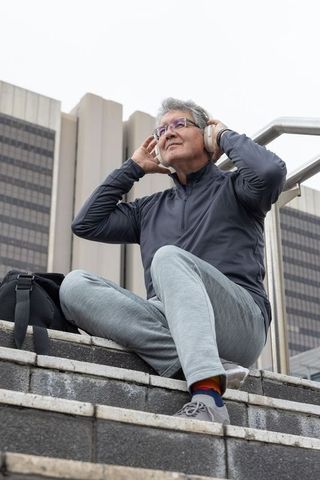 Senior man sitting on urban steps wearing wireless headphones and athletic wear relaxing