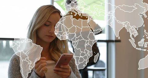 Young woman tapping pink smartphone in cafe with world map overlay for travel planning