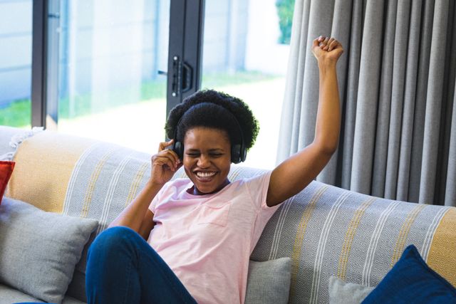 Happy african american mid adult woman enjoying music through headphones at home. unaltered, lifestyle, domestic life, joy, leisure.