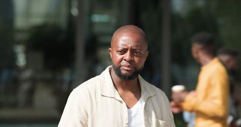 African american man walking urban plaza wearing beige overshirt looking thoughtful