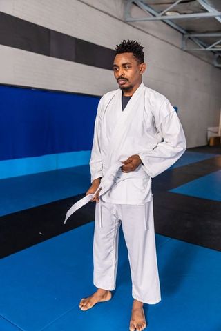 Man in white gi adjusting belt standing inside dojo