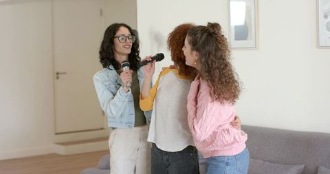 Three friends singing and hugging in cozy living room holding handheld microphones