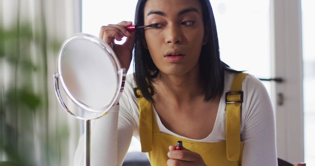 Transgender person focusing on applying eye makeup with a brush in front of a mirror. Can be used for articles on beauty routines, self-expression, transgender visibility, makeup tutorials, and personal grooming.