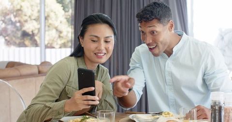 Couple sharing surprise while checking phone over casual breakfast at cozy home table