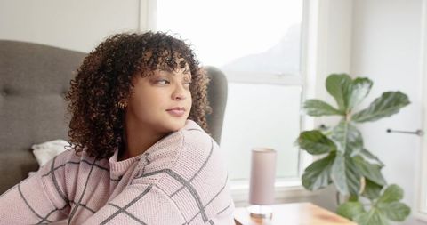 Serene woman gazing out window in cozy pink sweater with fiddle leaf fig