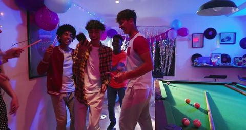 Diverse Friends Celebrating with Glow Sticks Around Pool Table in Neon Party Night