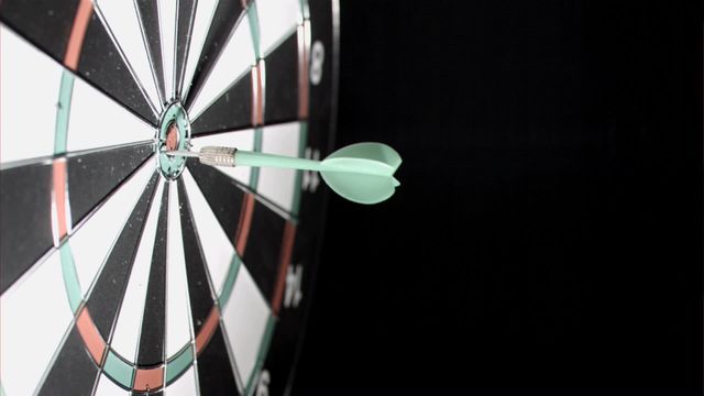 Dart striking precisely at the bullseye on a traditional dartboard is showcased against a dark backdrop. Symbolizing concepts of success, accuracy, precision, and hitting goals. Ideal for illustrations in competitive sports environments, success stories, strategic planning presentations, or motivation-related materials.