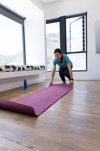 African american woman unrolling purple yoga mat for home workout in bright modern room