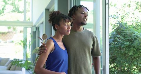 African american couple embracing by sliding glass door looking out to sunlit garden