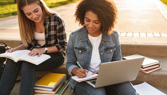 College students studying together on campus steps at sunset with laptop and notebooks