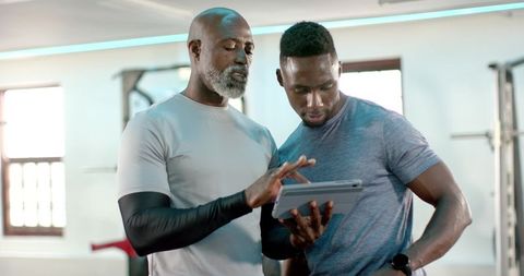 African american senior trainer coaching client with tablet in gym for fitness plans