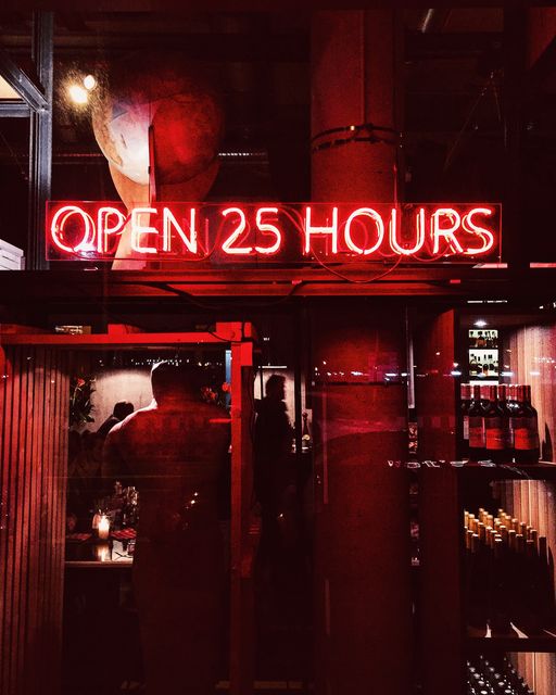Retro neon sign reading 'OPEN 25 HOURS' displayed inside a bar or restaurant, showcasing vibrant and inviting nightlife ambiance. Useful for marketing materials related to nightlife, bar advertisements, vibrant urban scenes, and unique dining experiences.