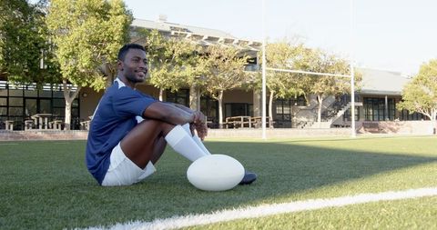 Rugby Player Sitting on Field with Ball in Tranquil Atmosphere