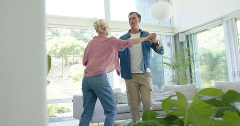 Dancing couple holding hands in bright modern living room with minimalist interior