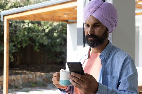Man in turban relaxing at home with mug and smartphone