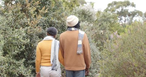 African american couple walking through lush shrubland wearing cozy knit scarves