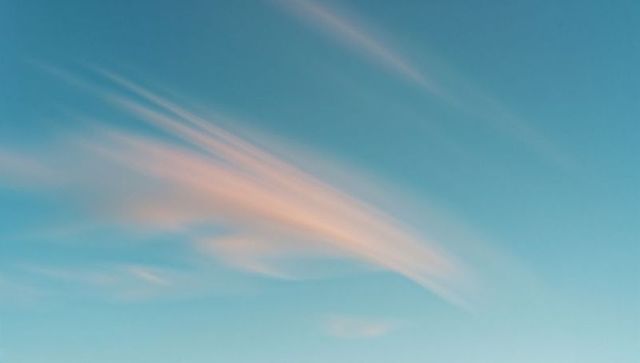 Dreamy pink pastel clouds drift across clear blue sky