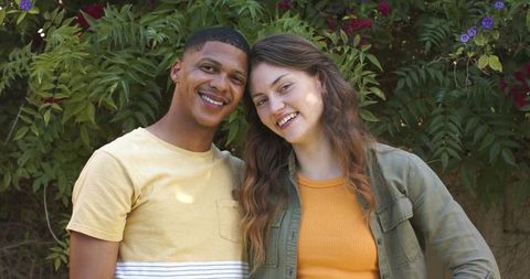 Young diverse couple smiling outdoors by vine wall wearing yellow and olive outfits