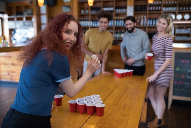 Portrait of smiling woman playing beer pong game with friends in bar