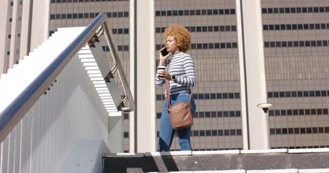 African American woman walking up urban stairway talking on smartphone holding coffee