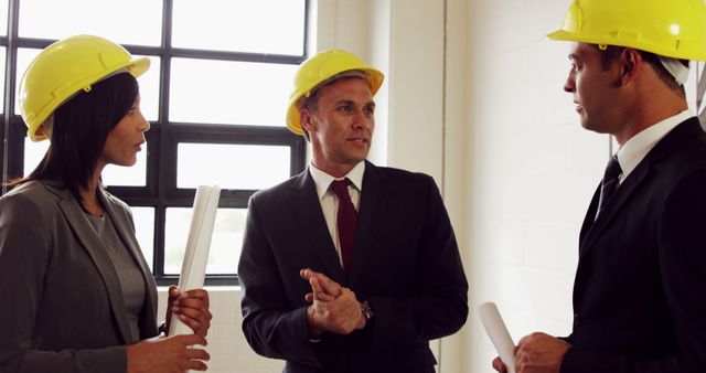 A diverse group of professionals, including a Caucasian woman and two Caucasian men, are engaged in a discussion, with copy space. They appear to be in the construction or engineering field, as indicated by their hard hats and formal attire.