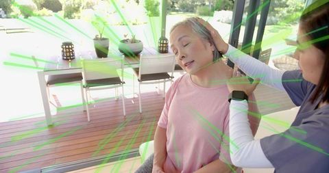 Nurse providing gentle neck support to senior Asian woman on sunlit deck