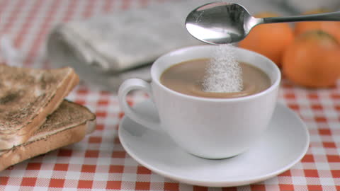 Sugar Pouring into Coffee at Breakfast with Toast and Oranges