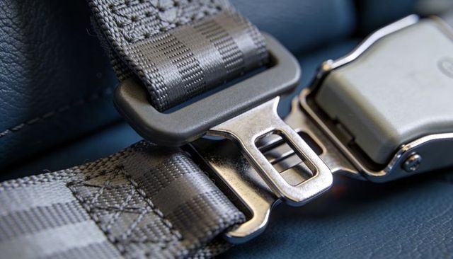 Locking metal seat belt buckle with woven nylon strap on dark blue leather cabin seat