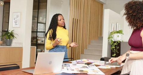 African american woman leading creative team meeting with laptop and design swatches