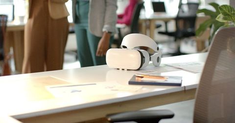 Diverse female coworkers discussing virtual reality headset in bright open office