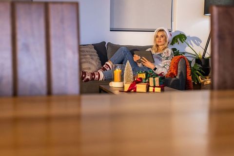 Young woman relaxing on couch wearing santa hat holding tablet with christmas gifts