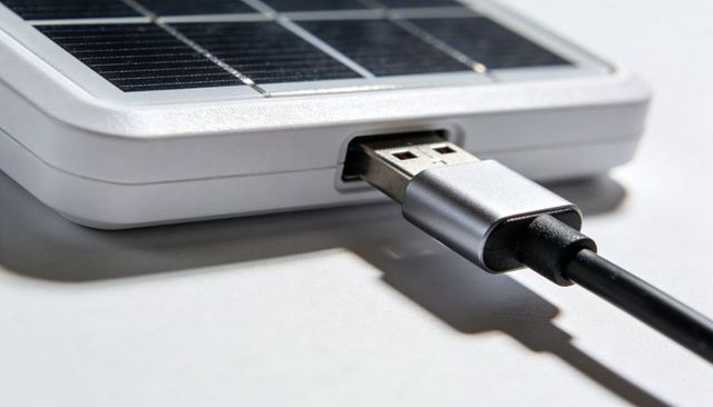 Close-up of usb-a cable plugging into portable solar charger on white tabletop with shadow