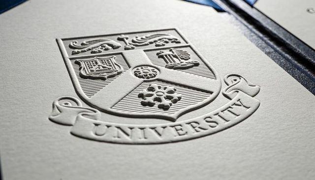 Embossed university crest on thick cream card with raised heraldic shield and ribbon