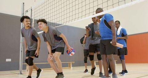 High school volleyball team huddling at net holding ball and clipboard during practice
