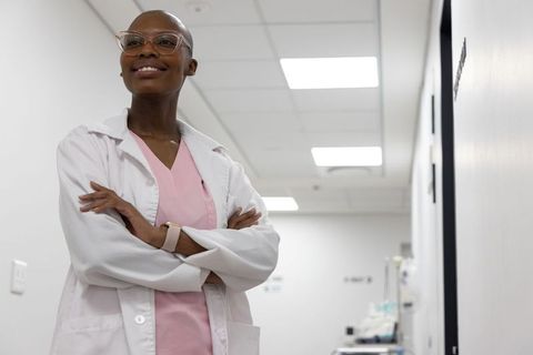 Confident african american clinician standing arms crossed in medical hallway wearing pink scrubs