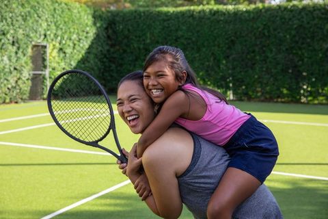 Mother and daughter playing on tennis court for fun family bonding