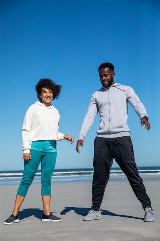 Friends stretching on sunny beach in athletic gear