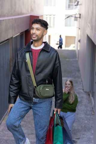 Young diverse shoppers walking up urban alley, man in leather jacket with green crossbody