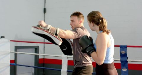 Female boxer practicing focus-mitt training with male coach in boxing ring