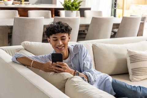 Relaxed Young Man Using Smartphone on Modern Couch in Bright Living Room