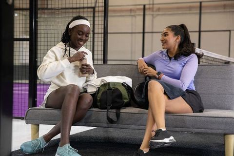 Diverse female teammates relaxing and chatting courtside at indoor tennis facility