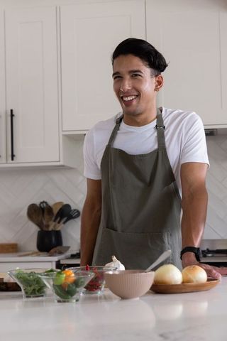 African american man preparing salad in modern minimalist kitchen wearing olive apron