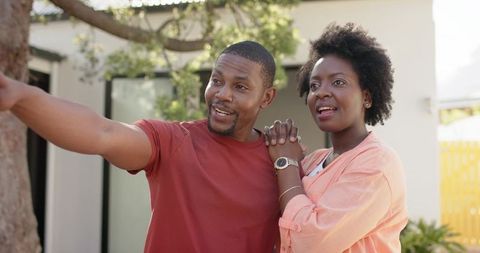 African american couple holding hands pointing and smiling in sunlit backyard