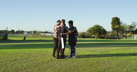 Teen male cricket teammates huddling on outfield before match, showing unity and focus