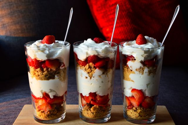Layered strawberry parfait features fresh strawberries, creamy layers, and crumbled biscuits in glasses. Ideal for dessert menus, food blogs, and cooking magazines. Great for promoting homemade recipes and delightful summer treats.