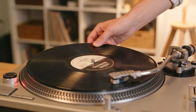 Hand placing vintage vinyl on turntable with tonearm ready for playback in cozy home