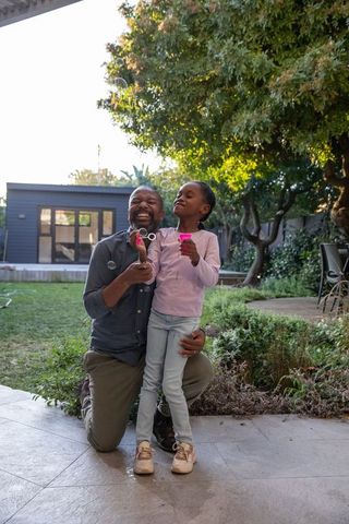 African american father playing bubbles with daughter on backyard patio