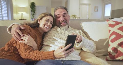 Couple smiling together on couch relaxing with smartphone