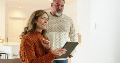 Couple Sharing Tablet in Cozy Modern Kitchen Wearing Cable-Knit Sweaters, Smiling Together
