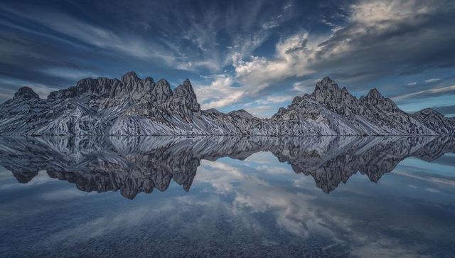 Snow-dusted alpine peaks mirroring on glassy lake at twilight